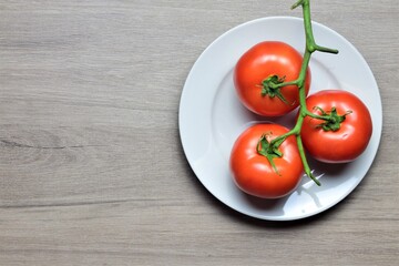 Red tomatoes on branch, on a white plate on a circular wooden table