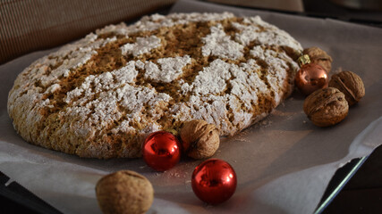 Früchtebrot backen, frischer Teig geht mit Nüssen und Christbaumkugel vor silbernem Hintergrund auf Backblech für Advent und Weihnachten	
