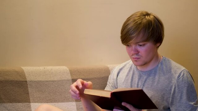 Portrait of a man turning a page of an old book and sitting on couch indoors. Concept. Caucasian male reader enjoying literature at home, reading, hobby, lifestyle concept.