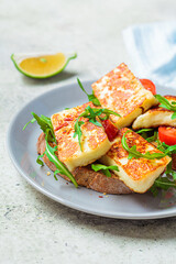 Fried halloumi sandwich with arugula and tomatoes on gray plate. Toast with grilled cheese and tomatoes.