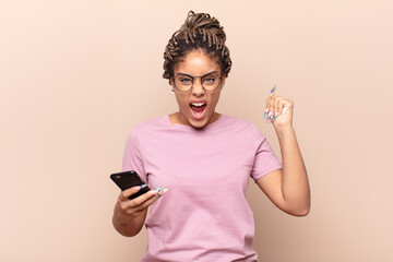 young afro woman shouting aggressively with an angry expression or with fists clenched celebrating...