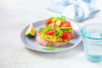 Tofu scrambled sandwich with avocado, arugula and tomato on gray plate. Healthy vegan food concept.