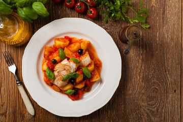 Traditionally prepared cod in Spanish. Served in tomato sauce with boiled potatoes, olivki and basil. Top view.