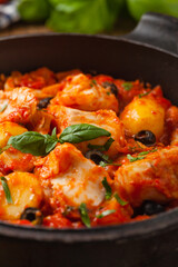Traditionally prepared cod in Spanish. Served in tomato sauce with boiled potatoes, olivki and basil. Front view.