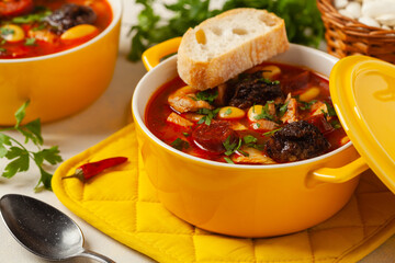 Traditional Spanish goulash soup. Fabada Asturiana. Served with a yellow clay pot with lid. Front...