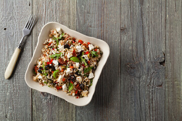 Trendy lunch with red rice, a mix of groats and vegetables. Top view. Served in white bowl on grey wooden background.