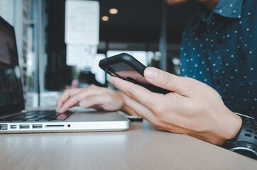 Man holding a cell phone and a laptop at a desk