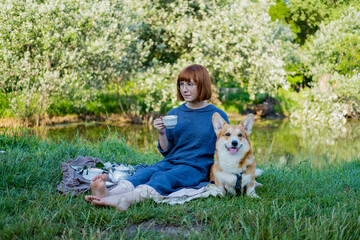 Young woman in retro dress with funny corgi dog on the picnic, female with cute dog drink english tea in the park