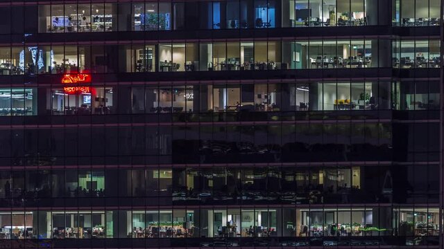 Modern office building with big windows at night timelapse close up view, in windows glowing light shines and some people inside, Singapore. Tilt down