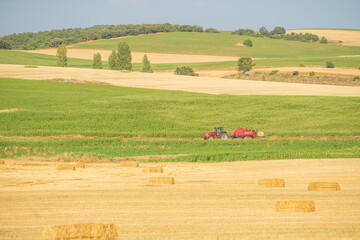 Picturesque summer landscape in the center of the Iberian Peninsula. Freshly mowed wheat field. The farmer collecting straw bales with his tractor.