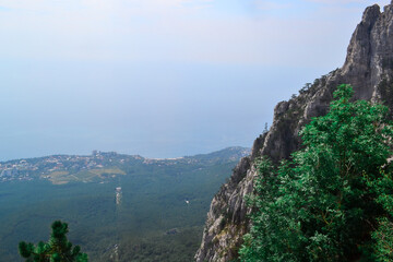 view of large stone rock with green trees stands on cliff against the backdrop of Black sea coast in Crimea, city is below
