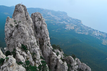 Fototapeta na wymiar large steep sharp stone rock Ai-petri with green trees stands on a cliff against the background of Black sea coastline in Crimea, the city below