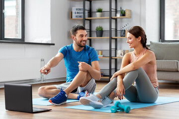 fitness, sport and technology concept - happy couple with laptop computer doing sports at home