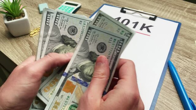 401k retirement plan, a man counts 100 dollar bills at a wooden table.