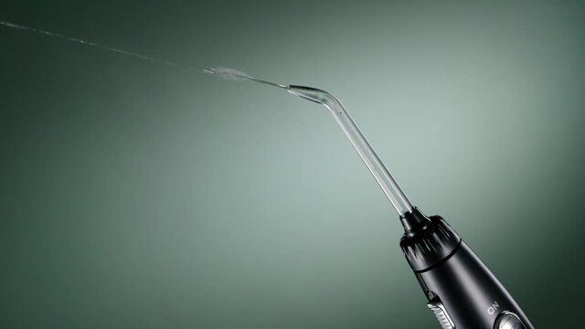 Black oral irrigator streams on green background. Working water flosser ready to clean teeth. Dental care, healthcare technology. Full HD 240 fps