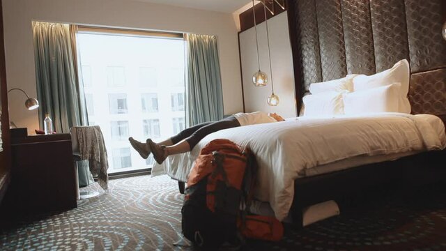 Woman tourist backpacker happy to stay in high quality hotel room after long trip. She jumping on the soft cozy bed.