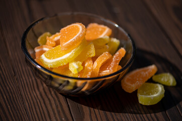 Marmalade lemon slices in a glass vase on a wooden table in the sunlight, close-up, selective focus.