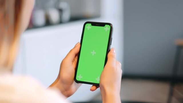 Young Woman Sitting On Sofa At Home And Uses IPhone With Green Screen Mock-up. 4k