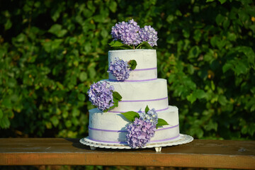 A photo of a wedding cake with violet colored flowers hydrangeas.