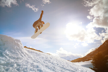 Young man in sunglasses makes a trick in flight with a snow kicker against the backdrop of mountains