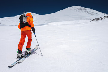 Ascent of a skier with a backpack in a mask and sunglasses on skis with poles to go uphill for...