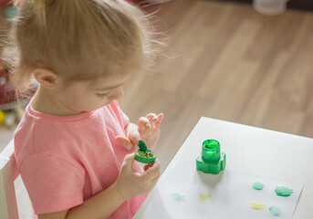 little girl drawing with fingerpaints , dunks his finger in the paints, color finger stamps.