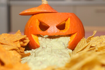 Carved pumpokin filled with guacamole and tortilla chips. Halloween party food. Selective focus.