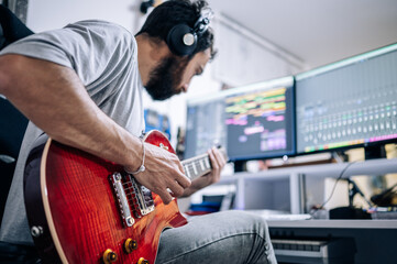 Young musician playing electric guitar with headphones at home studio. Music and professional...