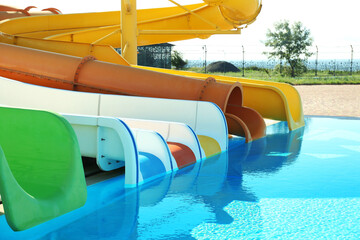 Different colorful slides and swimming pool in water park on sunny day