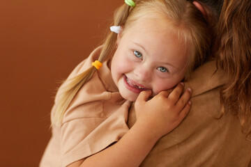Close up of mother holding happy daughter with down syndrome while standing against plain brown background in studio