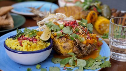 Vegan street food in trendy Asian style. Creamy coconut thai curry served in a pineapple with a rice on a side.