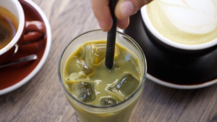 Top view of hand stirring matcha ice green tea with plastic straw. Vegan refreshing beverages 