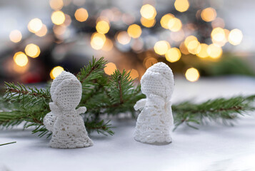 Fir tree branches and white crocheted angels on light background with bokeh. Christmas hamdmade gift concept.