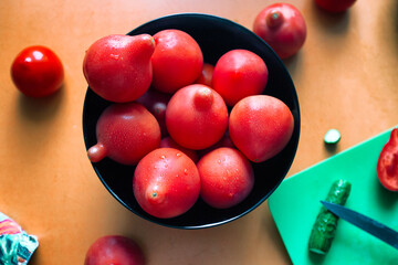 Red ripe tomatoes with water droplets  in a black bowl on orange kitchen table. Close up, selective focus