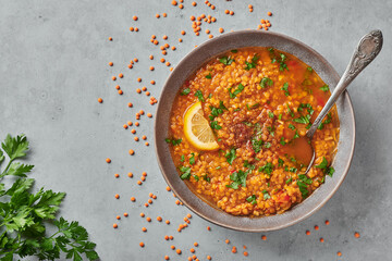 Red lentils tomato soup with parsley and lemon in gray plate on concrete table top. Vegetarian dish. Copy space