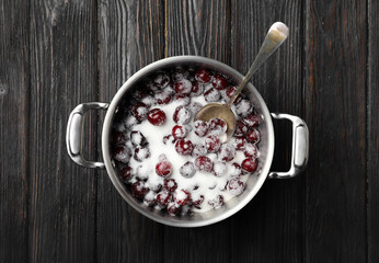 Pot with cherries and sugar on black wooden table, top view. Making of delicious jam