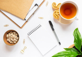 Home workspace: craft notebook, potted plant, pencil, cup of tea, paper clips. Cozy flat lay in pastel colors, feed on top, copy space.