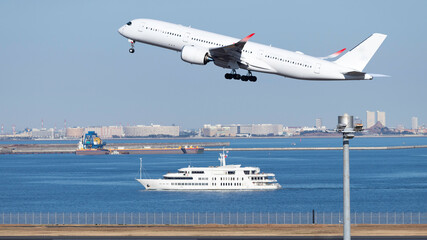 青空を背景に羽田空港を離陸するジャンボジェットと海を航行する客船