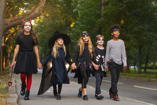 Full length portrait of multi-ethnic group of kids walking in street while trick or treating on Halloween