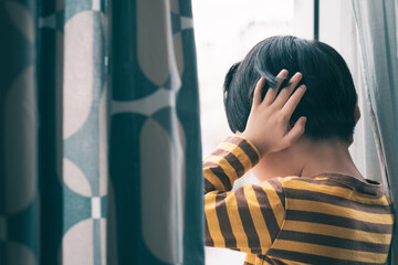 Little Asian boy stand by window, cry and cover ears feeling fear, insecure, anxiety and stress. Domestic Violence, Autism disorder spectrum awareness and Childhood mental disorders problem concept.