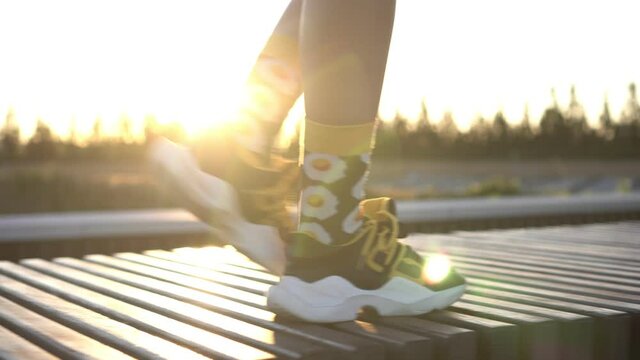 A woman in sports shoes walks against the backdrop of the sunset. Women's feet walk in sneakers