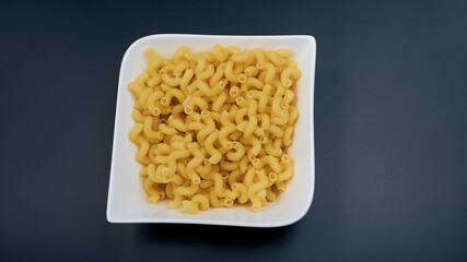 small spring-shaped pasta. Pasta in a white plate, a plate with macaroni on a dark table.