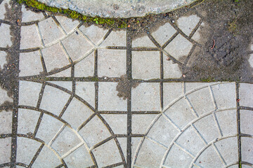 Decorative tiles on pavement with green grass growing through cracks
