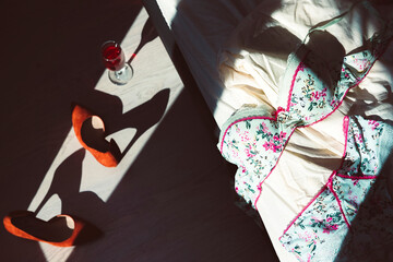 Beautiful set of female underwear in the rays of window light with red high-heeled shoes and a glass of wine.