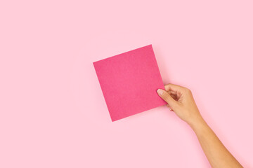 Mano de mujer sosteniendo un papel vacio de color rosa sobre un fondo rosa liso y aislado. Vista de...