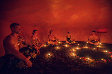 Group of people inside Mayan Temazcal- traditional steam sauna bath of Mesoamerican cultures. Diverse multiethnic people sitting around candle lights in circle in darkness and meditating - 379607240