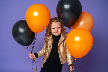 stylish little girl with curly hair in gold jacket with orange, black balloons