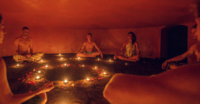 Group of people inside Mayan Temazcal- traditional steam sauna bath of Mesoamerican cultures. Diverse multiethnic people sitting around candle lights in circle in darkness and meditating