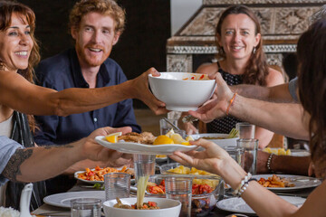 Diverse group of multiethnic friends enjoying meal sharing and passing food to each other in outdoor cafe or home. Leisure, food and drinks, people and holidays concept