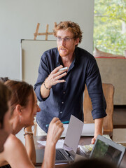 Cheerful young coach man standing near whiteboard for outdoor conference. Confident speaker training diverse employees group at tropical workshop or seminar